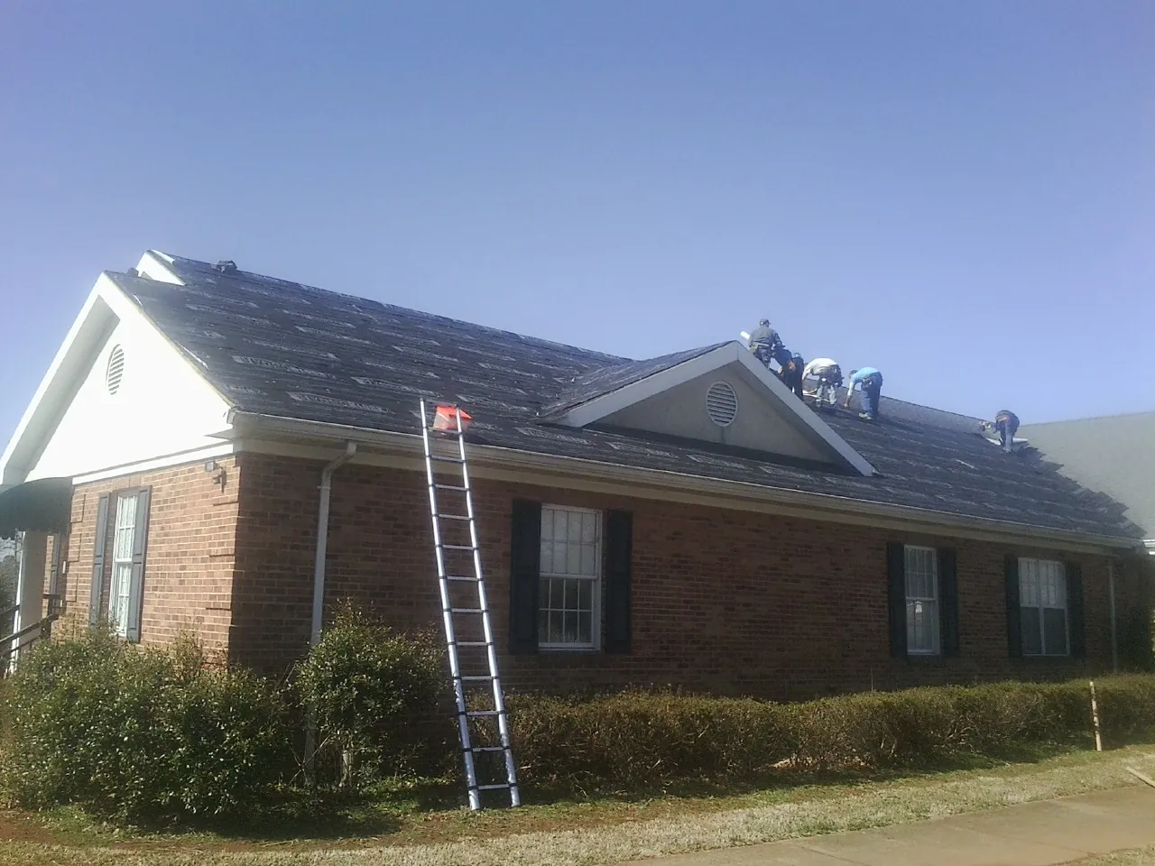 Crew tearing shingles off a brick ranch roof with a ladder set — Emergency Roof Repair work by our crew in Kinsman