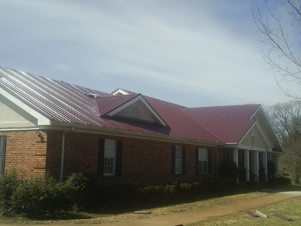 Red metal roof with gabled entries on a long brick building, from a Hail Damage Roof Repair job in Kinsman