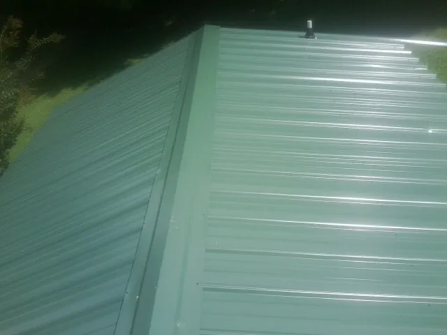 New green metal panels meeting at the ridge of a roof — Flat Roof Repair work by our crew in Kinsman