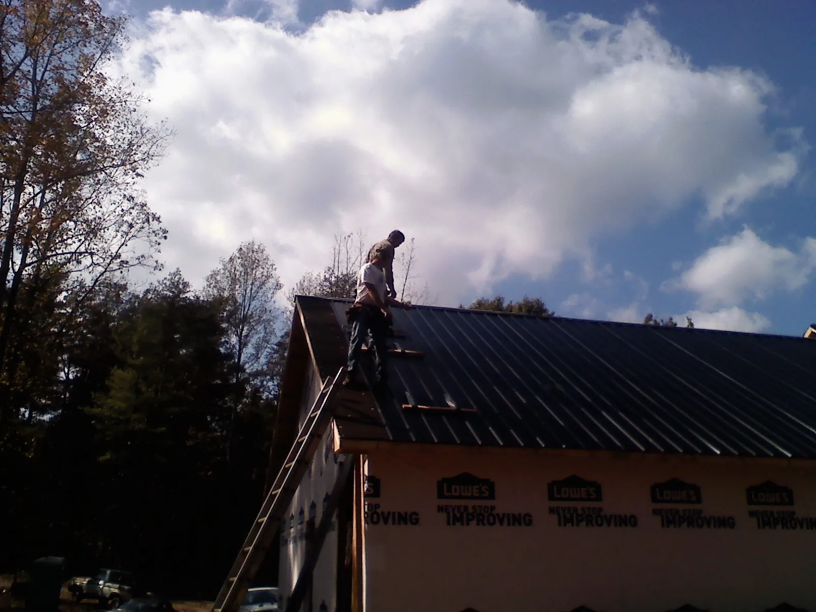 Roofer fastening dark metal panels high against a cloudy sky, from a Roof Inspection job in Kinsman