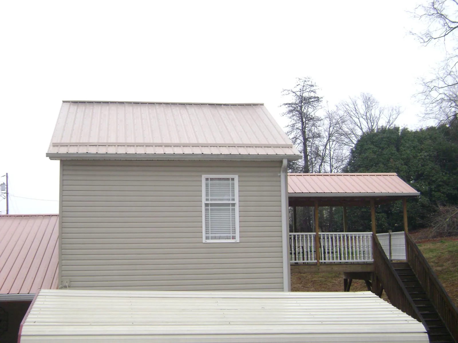 Tan metal roofs on a two story addition and attached porch, from a Roof Replacement job in Kinsman